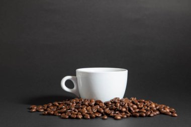 Siyah bir fonda kahve çekirdeği yığını üzerinde bir fincan kahve..