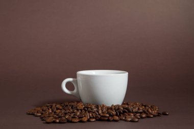 Kahverengi bir fonda kahve çekirdeği yığını üzerinde bir fincan kahve..