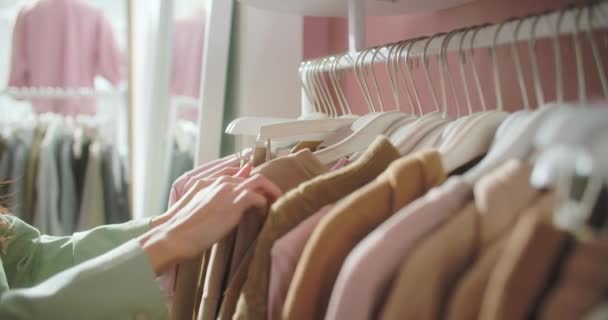 Close-up van vrouwelijke handen geplukt hanger kiezen van kleding in een kledingwinkel. Brunette Woman Hand Runs Over een Rack of Clothes Kopen van kleding in een winkelcentrum. Sale Promotie en Shopping Concept. — Stockvideo