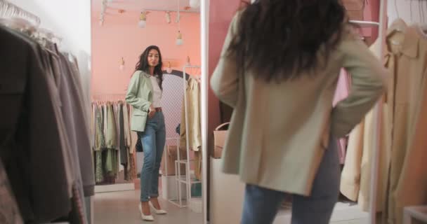 A Back View Shooting of a Brunette Woman Buyer Being in a Clothing Shop Staande voor de spiegel en het passen van een Clothers — Stockvideo