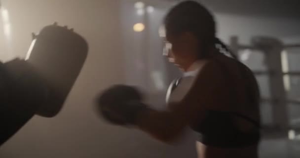 Młoda kobieta w rękawiczkach bokserskich i ubraniach sportowych boksuje ze swoim zręcznym trenerem. Unikają ciosów podczas treningu na ringu bokserskim. — Wideo stockowe