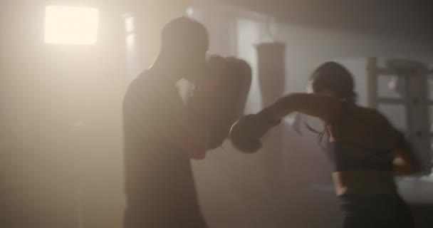 Mujer joven atleta en guantes de boxeo y ropa deportiva es el boxeo con su entrenador hábil. Esquivando golpes mientras practican en el ring de boxeo. — Vídeos de Stock