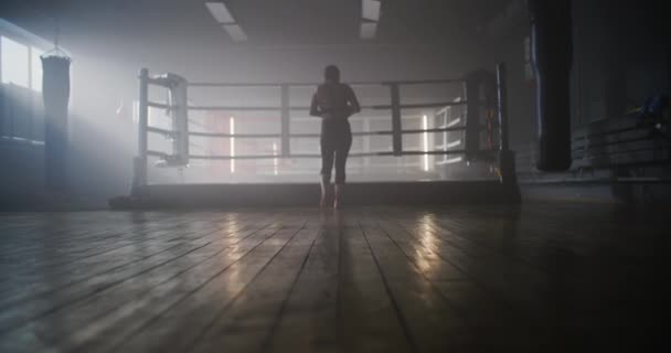 Kaukasische junge sportliche Frau mit brünetten Haaren übt im Boxring. Sportlerin trainiert im Fitnessstudio, macht einen Schattenkampf, bereitet sich auf einen Wettkampf vor. — Stockvideo