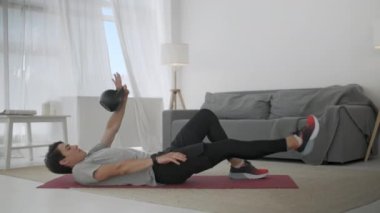 Gri tişörtlü yakışıklı genç adam ve siyah şortlu adam internette spor yapıyor. Güçlü Atletik Erkek Geniş ve Güneşli Oturma Odasında Çapraz Çatırtı Egzersizleri Yapıyor.