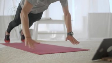 Gri tişörtlü yakışıklı genç adam ve siyah şortlu adam internette spor yapıyor. Yakışıklı Adam Evdeki Oturma Odasında Egzersiz Yapıyor ve şınav çekiyor.