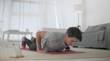 Gri tişörtlü yakışıklı genç adam ve siyah şortlu adam internette spor yapıyor. Yakışıklı Adam Evdeki Oturma Odasında Egzersiz Yapıyor ve şınav çekiyor.