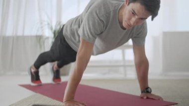 Gri tişörtlü yakışıklı genç adam ve siyah şortlu adam internette spor yapıyor. Karantina sırasında Hhome 'da Tahta Yapan Çekici Erkek Egzersizi.