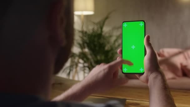 Cámara de mano: Vista posterior del hombre que sostiene la clave de croma Pantalla verde Smartphone Ver contenido sin tocar o deslizar. Niño que usa el teléfono móvil, navegar por Internet, ver contenido — Vídeos de Stock