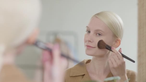 Aantrekkelijke Blond vrouw gezicht de spiegel make-up mooie meisje make-up. Jonge vrouw blozen op het gezicht met behulp van make-up borstel vol zelfvertrouwen Kijken naar spiegel — Stockvideo