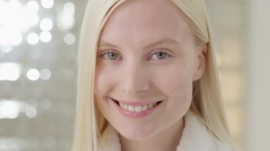 Banyo havlusu takan, uzun sarı saçlı beyaz bir kadın, parlak bir banyoda kameraya bakıyor. Cilt bakımı spa prosedürlerinin reklamını yapmak. Yakın plan portre