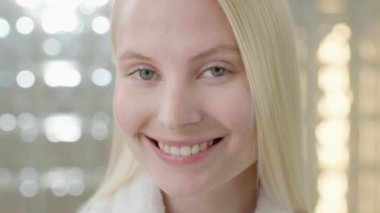 Banyo havlusu takan, uzun sarı saçlı beyaz bir kadın, parlak bir banyoda kameraya bakıyor. Cilt bakımı spa prosedürlerinin reklamını yapmak. Yakın plan portre