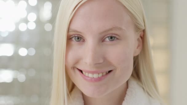 Jonge blanke vrouw met lang blond haar dragen van een badhanddoek Kijken naar camera in een heldere badkamer. Reclame voor huidverzorging spa procedures concept. Close-upportret — Stockvideo