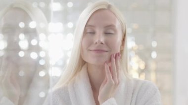 Çekici Sarışın Kadın 'ın portresi Doğal Makyajlı Bornoz Giyen Kameraya Bakıyor ve Yüzüne Dokunuyor. Yakın plan portre