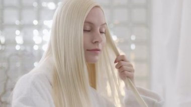 Kameraya bakan, doğal makyajlı, çekici sarışın bir kadının portresi. Parlak Banyo 'da saç stili yapan kendinden emin bir kadın. Kapat.