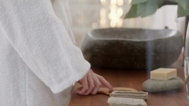 Uzun sarı saçlı, banyo havlusu takan, aynaya bakan ve parlak bir banyoda sağlıklı düz saçlarla savaşan beyaz kadının yakın çekimi. Yavaş Hareket