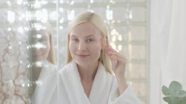 Parlak Banyo 'da yüz masajı yapan güzel bir kadın. Ağır çekim. Çekici Sarışın Kadın Portresi Roller Masajlı Bornoz Giyen Yüzüne Masaj Yapan ve Kameraya Bakan