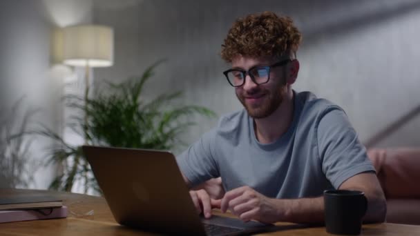 Молодой мужчина фрилансер в очках, смотрит на экран ноутбука, работает дистанционно дома. Мужские глаза в очках Поздно ночью Прокрутка перед ноутбука Интернет-серфинг — стоковое видео