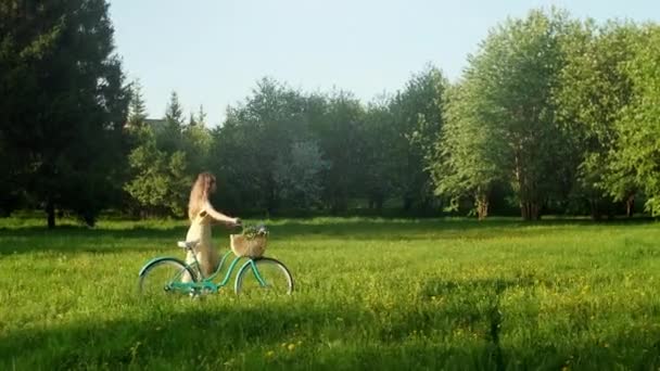 Radfahrerin Frau zu Fuß mit dem Fahrrad auf der Landstraße zur Sommerzeit.Schöne Radfahrerin im Kleid Radfahren auf dem Fahrrad auf dem Feldweg Grünes Grasfeld Spaß haben und das Leben genießen. — Stockvideo