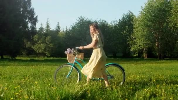Glückliche junge Frau zu Fuß mit einem Fahrrad mit Blumenkorb auf der Landstraße im Sommer bei Sonnenaufgang. Schöne Frau am Boden Pfad Green Grass Field Spaß haben und das Leben genießen — Stockvideo