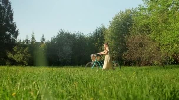 Fietser vrouw lopen met de fiets op het platteland weg in de zomer tijd.Mooie vrouw fietser in jurk fietsen op de fiets op de begane grond pad groen grasveld plezier hebben en genieten van het leven. — Stockvideo