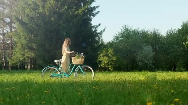 Glückliche junge Frau zu Fuß mit einem Fahrrad mit Blumenkorb auf der Landstraße im Sommer bei Sonnenaufgang. Schöne Frau am Boden Pfad Green Grass Field Spaß haben und das Leben genießen — Stockvideo