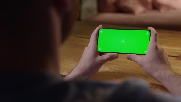 El kamerası: Young Man in Home Sitting on a Wood Desk kullanırken Green Mock-up Screen Smartphone 'u kullanıyor. Oğlan Dokunmadan İçerik Ekranı İzliyor. — Stok video