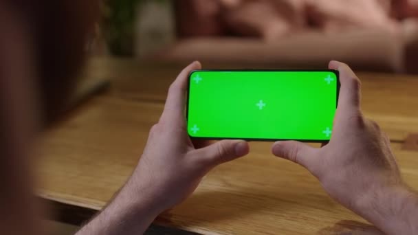 Handheld Camera: Jongeman thuis met Chroma Key Green Screen Smartphone Content bekijken zonder aanraken of vegen. Surfen op internet, Content bekijken, Video 's — Stockvideo