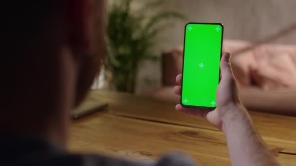 Φορητή κάμερα: Νεαρός στο σπίτι κρατώντας Chroma κλειδί πράσινη οθόνη Smartphone Watching Περιεχόμενο χωρίς να αγγίξετε ή να Swiping. Περιήγηση στο Internet, Παρακολούθηση περιεχομένου, Βίντεο — Αρχείο Βίντεο
