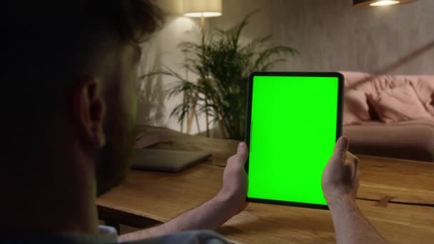 Kamera ręczna: Przez ramię Zobacz młodego człowieka w domu za pomocą zielonej Mock-up ekranu Tablet. Podlewanie zawartości bez dotykania ekranu gadżetu. Przeglądanie Internetu. — Wideo stockowe