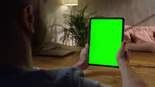 Портативная камера: над плечом Просмотр Молодой человек дома, используя с зеленым макетом экрана планшета. Смотреть контент, не касаясь экрана гаджета. Просмотр Интернета. — стоковое видео