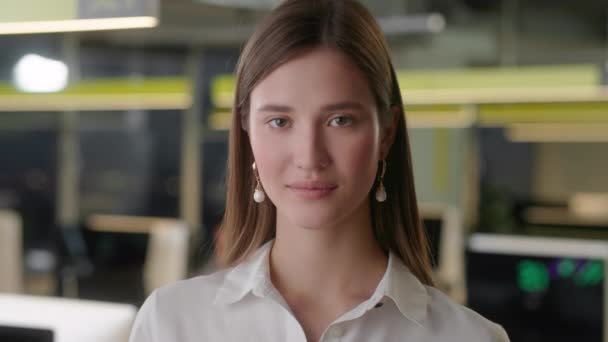 Elölnézetből gyönyörű fiatal nő professzionális viselő fehér ing. Egy fiatal női irodavezető portréja, aki kamerába néz és jó hangulatban van. Elmosódott irodai háttér. — Stock videók