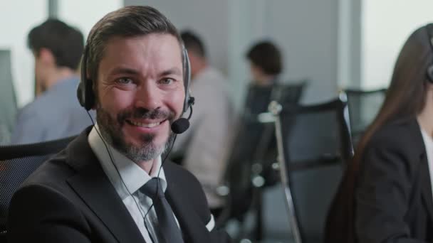 Retrato de guapo feliz y hombre sonriendo y mirando a la cámara mientras trabajaba en Call Center. Utilice la PC de escritorio en la mesa de la computadora y la línea telefónica en el co-trabajo moderno. — Vídeos de Stock