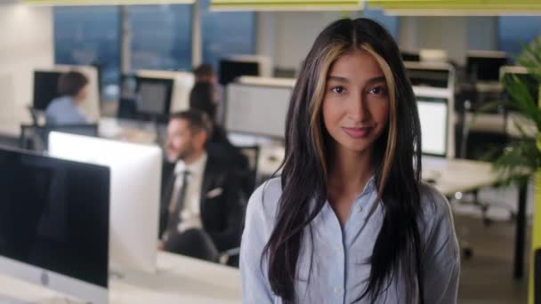 Elölnézetből gyönyörű fiatal nő professzionális viselő kék ing. Egy fiatal női irodavezető portréja, aki kamerába néz és jó hangulatban van. Elmosódott irodai háttér. — Stock videók