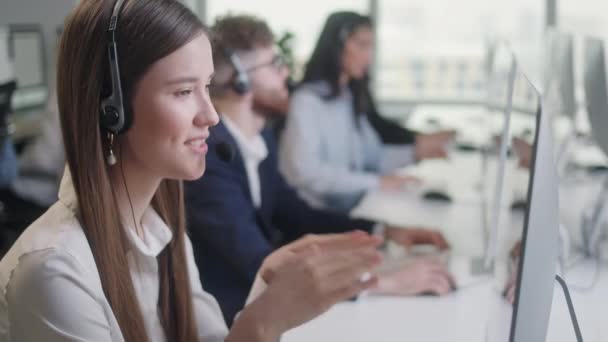 Κοντινό πλάνο Πορτρέτο Γυναίκα ενός ειδικού τεχνική υποστήριξη πελατών Μιλώντας σε ένα ακουστικό, ενώ εργάζονται σε έναν υπολογιστή σε ένα τηλεφωνικό κέντρο. Διαφορετική ομάδα εργαζομένων μιλά στην ανοικτή γραμμή πώλησης. — Αρχείο Βίντεο