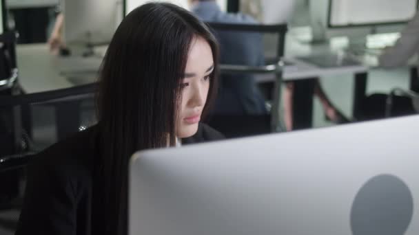 Привлекательная молодая женщина, работающая за настольным компьютером во время работы в большом офисе в открытом космосе. Портрет позитивной деловой женщины, смотрящей на экран компьютера в помещении. — стоковое видео