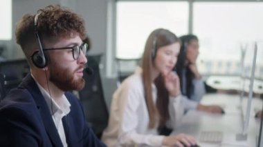 Çağrı merkezinde bir bilgisayar ve 7 / 24 yardımcı müşteri hizmetleri üzerinde çalışırken kulaklıkla konuşan bir teknik müşteri destek uzmanının portresi. Bilgisayar tablosu ve telefon hattında masaüstü bilgisayarı kullan