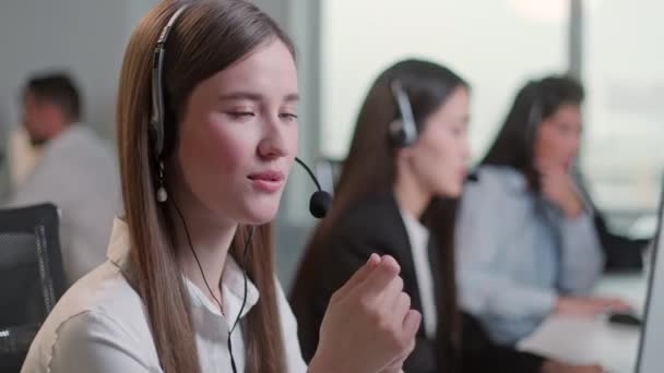 Close Up Retrato Mujer de un especialista en soporte técnico al cliente Hablando con un auricular mientras trabaja en un ordenador en un centro de llamadas. Diverso grupo de trabajadores habla en línea directa de venta. — Vídeo de stock