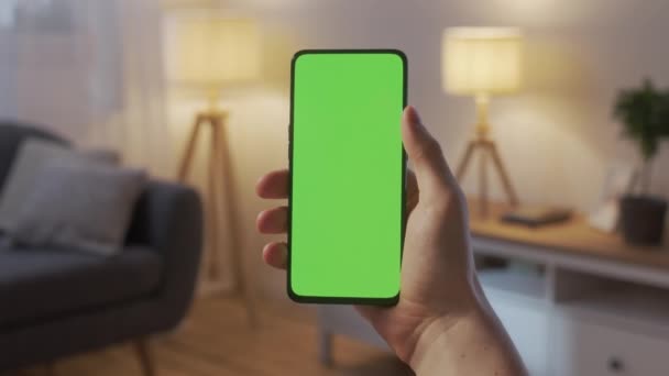 Punto de vista de un hombre joven en casa sentado en la sala de estar por la noche usando con Green Mock-up Screen Smartphone. Boy está viendo contenido sin tocar la pantalla del gadget. — Vídeos de Stock