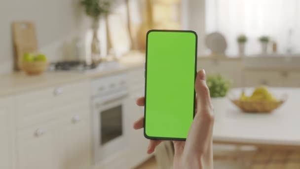 Точка зору молодої жінки вдома сидить на кухні, використовуючи з зеленим макет екрану смартфона. Жінка розміщує контент, не торкаючись екрана гаджетів. Модифікована технологія — стокове відео