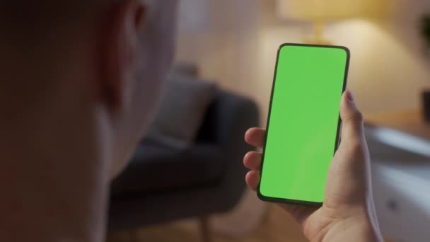 Back Pohled na člověka v obývacím pokoji Sedí na židli pomocí telefonu s Green Mock-up Screen Chroma Key bez bodů Surfování Internet Sledování obsahu Videa Blogy. Klepnutí na prostřední obrazovku — Stock video