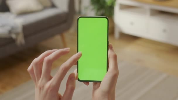 Tocando en la pantalla central. Vista posterior de la mujer en la sala de estar sentada en una silla usando el teléfono con la clave de croma de pantalla falsa verde sin puntos de seguimiento Navegar por Internet Ver contenido Videos Blogs. — Vídeos de Stock