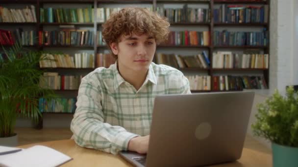 Hombre de estudiante atractivo usando el ordenador portátil Buscar información Curso de Internet Estudiar en línea e Aprender en la aplicación Buscando en el monitor del ordenador portátil Hacer investigación para el examen de prueba Sentarse en el escritorio de la biblioteca — Vídeo de stock