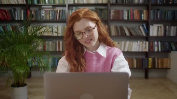 Привлекательная студентка женщина с помощью ноутбука Поиск информации Интернет-курс онлайн обучение в приложении Глядя на ноутбук монитор делает исследования для тестирования экзамен сидеть за столом библиотеки и улыбка — стоковое видео