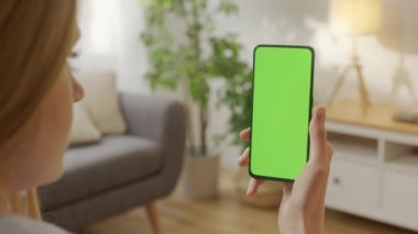 Oturma odasındaki kadının Yeşil Model Ekran Kroma Anahtarı ile Telefon kullanarak İnternet İzleme İçerik Videoları Blog 'larında gezinirken ki görüntüsü. Sola İki Kere Kaydırma.