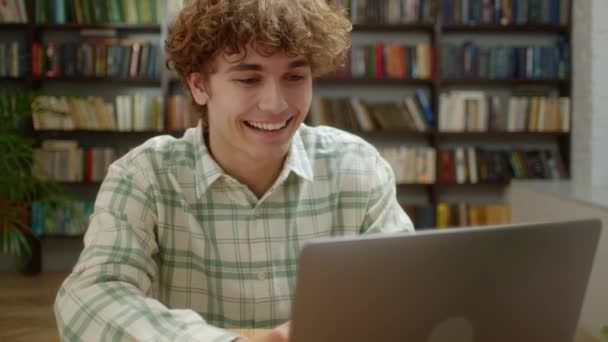 Hombre de estudiante atractivo usando el ordenador portátil Buscar información Curso de Internet Estudiar en línea e Aprender en la aplicación Buscando en el monitor del ordenador portátil Hacer investigación para el examen de prueba Sentarse en el escritorio de la biblioteca y sonreír — Vídeo de stock