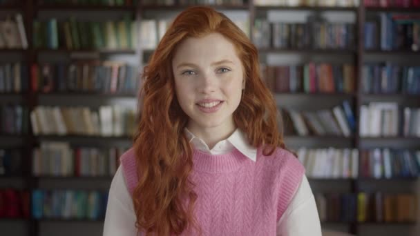 Portret van een roodharige studente die voor de camera staat en lacht in de bibliotheek van de middelbare school. Onderwijs, Literatuur en Mensen Concept. — Stockvideo