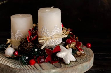 Yeni yıl dekorasyonu ya da Noel masası. Noel ağacı dalları, suni çiçekler ve yakın plandaki tahta tepside üç beyaz mum.