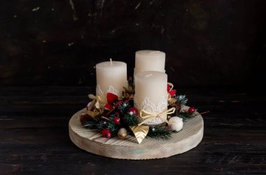 Yeni yıl dekorasyonu ya da Noel masası. Noel ağacı dalları, suni çiçekler ve yakın plandaki tahta tepside üç beyaz mum.