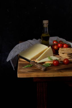 Taze sert peynir, bıçak, kiraz domatesleri ve krakerler ahşap bir masada yakın plan.