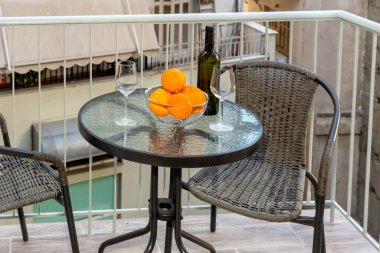 Masada iki boş bardak, bir şişe beyaz şarap ve bir kase portakal var.